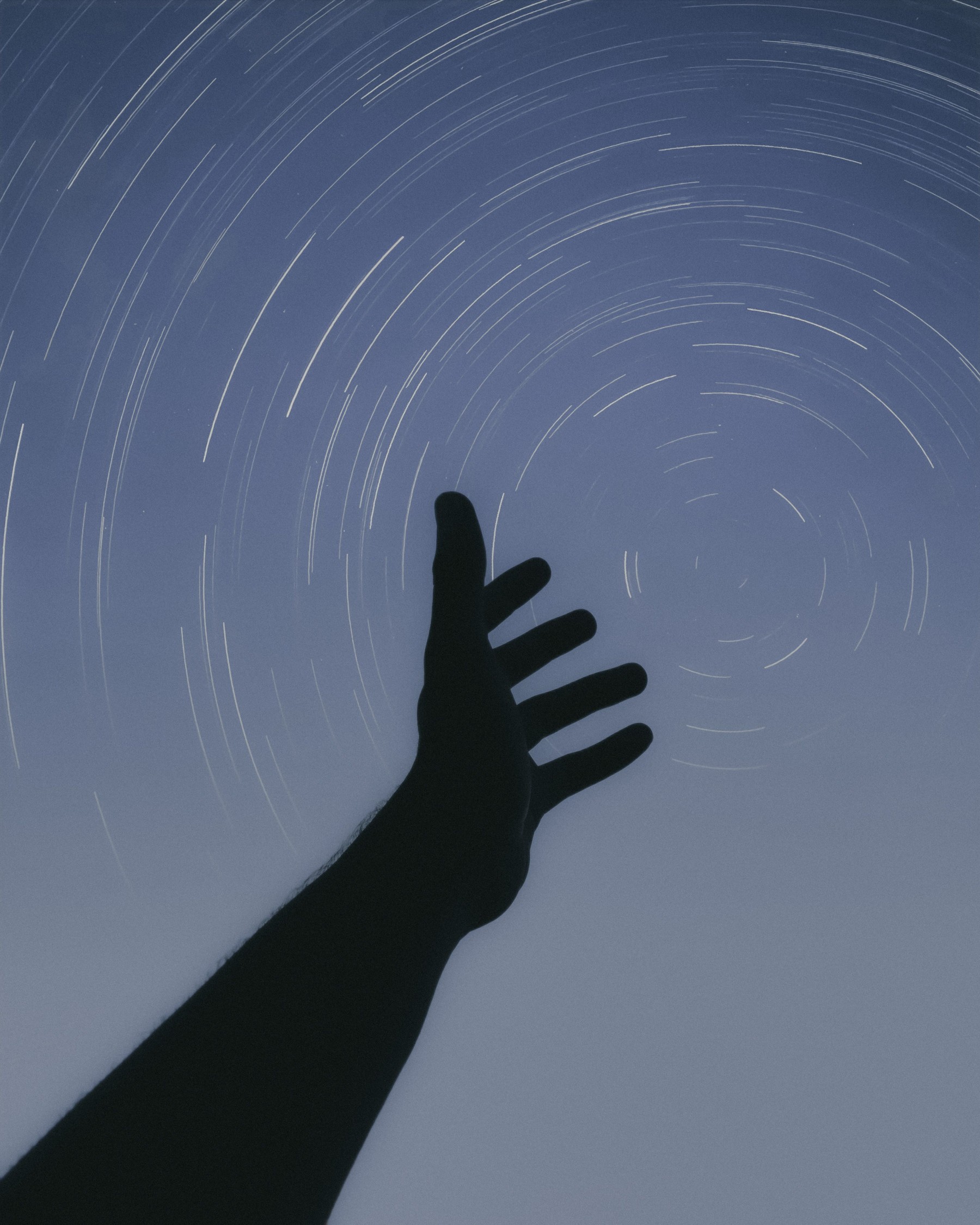 A hand reaching toward circular star trails in the night sky