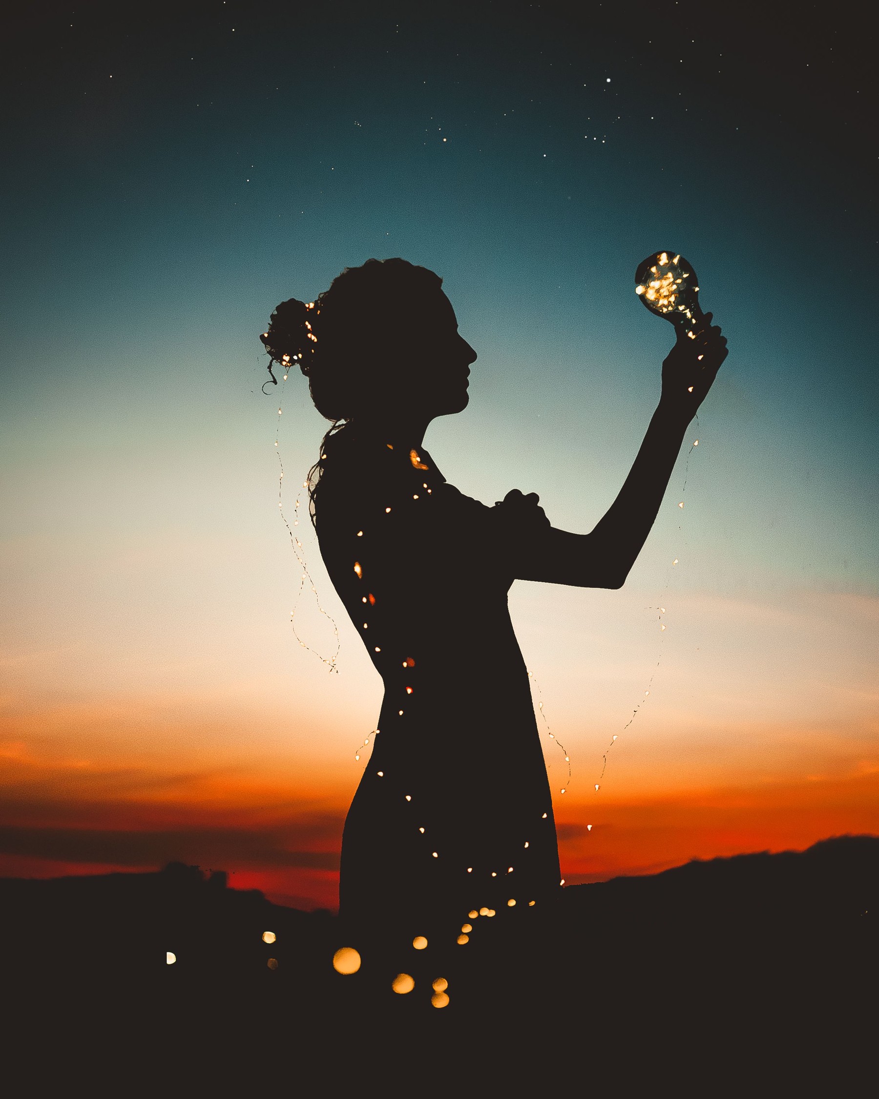 A silhouetted figure holding a light against a sunset sky