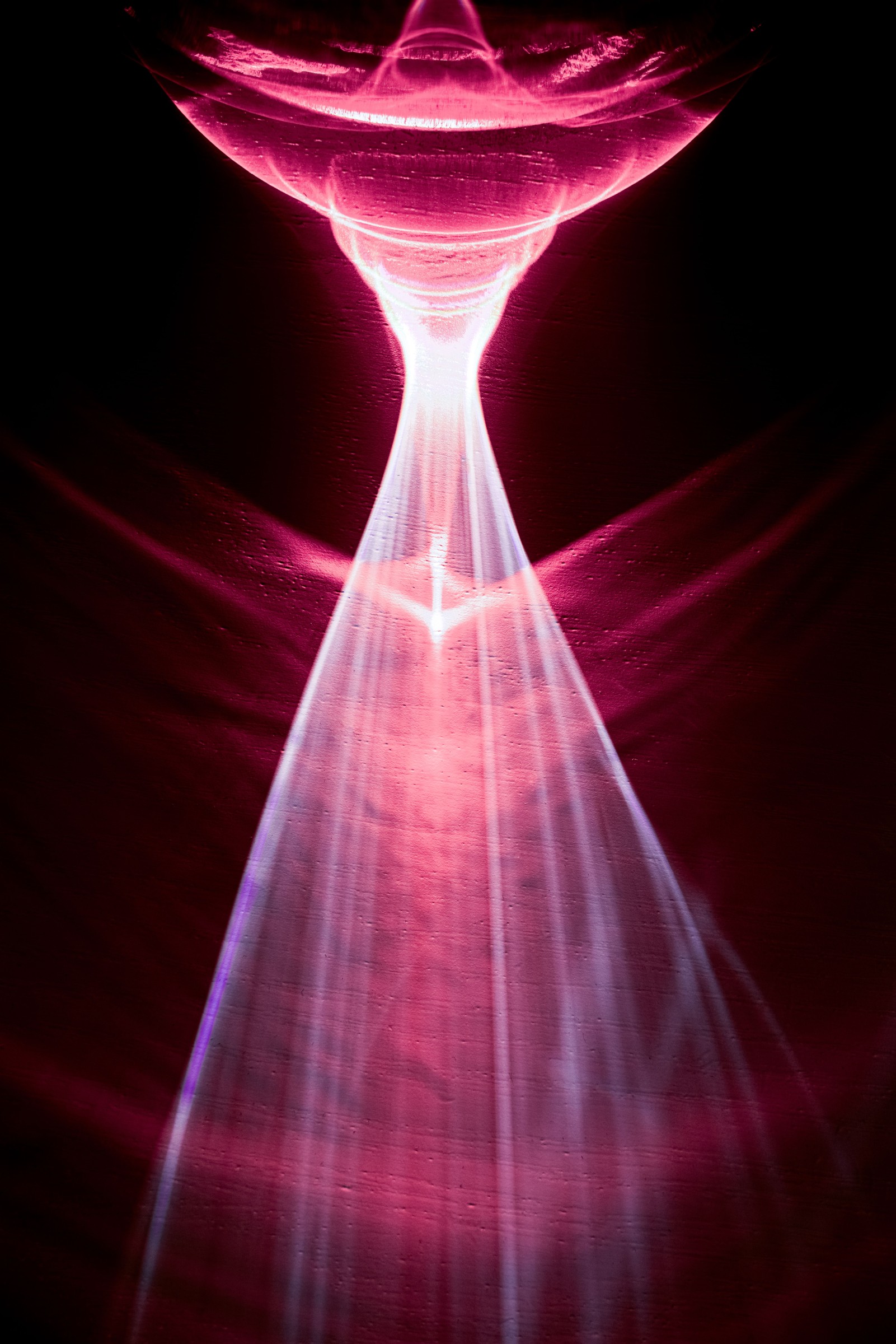 An abstract pink light pattern with flowing waves and a bright central beam