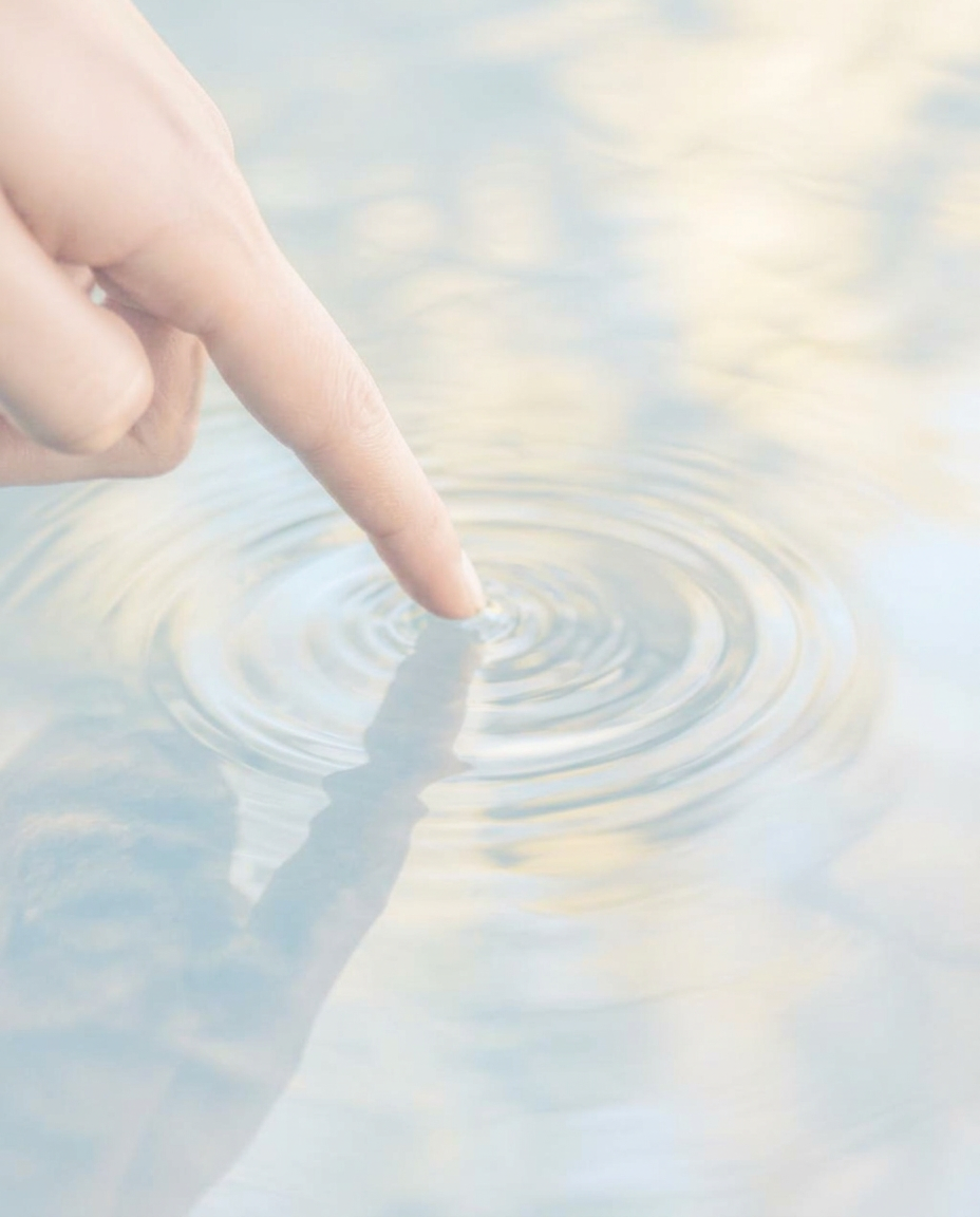 A fingertip touching still water, sending out soft ripples